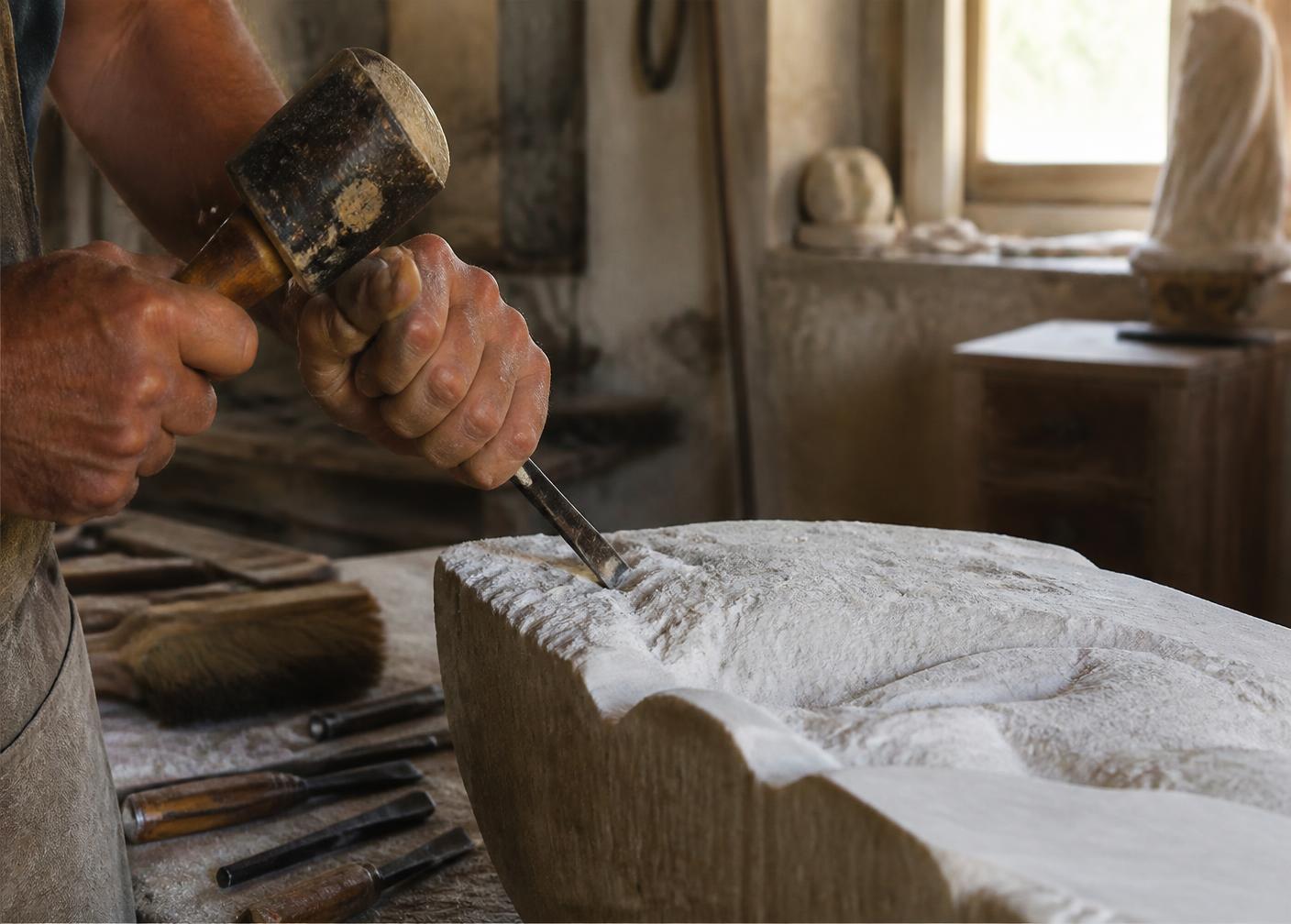 An artisan's hands carving stone with a mallet and chisel.